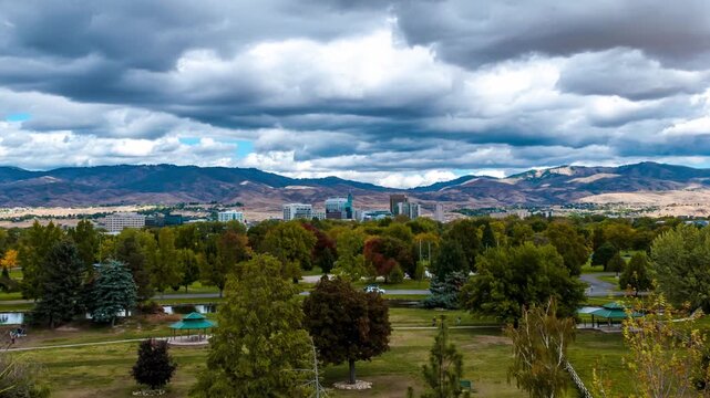 Ann Morrison Park Boise Timelapse Drone Shot Featuring Lush Greenery Vibrant Autumn Trees a Serene Pond and a Distant City Skyline Under a Dramatic Moving Cloudscape in 4k Resolution