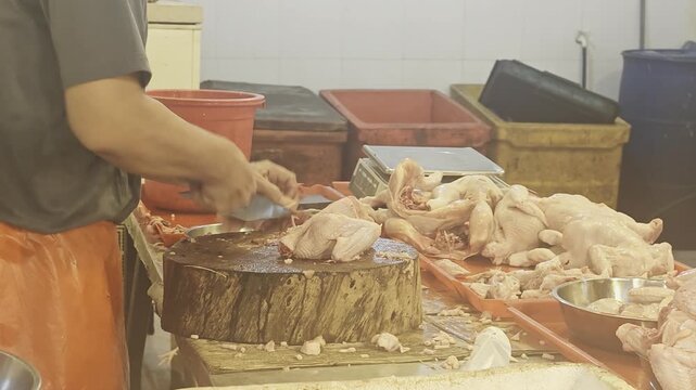 a local butcher using a cleaver to chop raw whole chicken carcasses on a heavy wooden cutting block at a traditional wet market stall