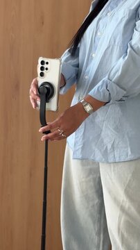 Close-up of a woman's hands mounting a white smartphone onto a tripod stick.