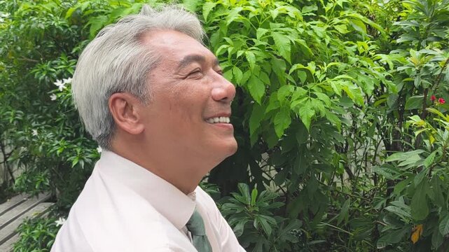 Relaxed happy carefree middle age old Asian business man breathing the clean, unpolluted air in green park, wellness concept image of good summer, summer wellness, sunlight exposure