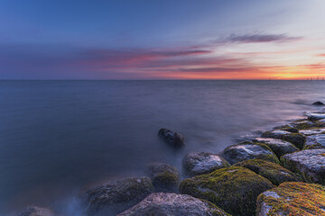 Naklejka premium Markermeer, Volendam, Netherlands. Long exposure technique creates a smooth, silky appearance on the water surface, while the moss-covered rocks in the foreground add texture, depth and visual interes
