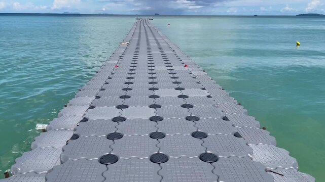 Floating modular pier stretching into calm turquoise water under dramatic clouds in Phuket, Thailand. Scenic tropical seascape with strong leading lines and a peaceful coastal atmosphere