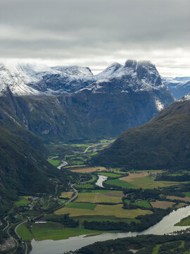 Aerial view of the Troll Wall mountain face rising above the lush green valley, winding river, and agricultural fields in Rauma Municipality, More og Romsdal, Norway.