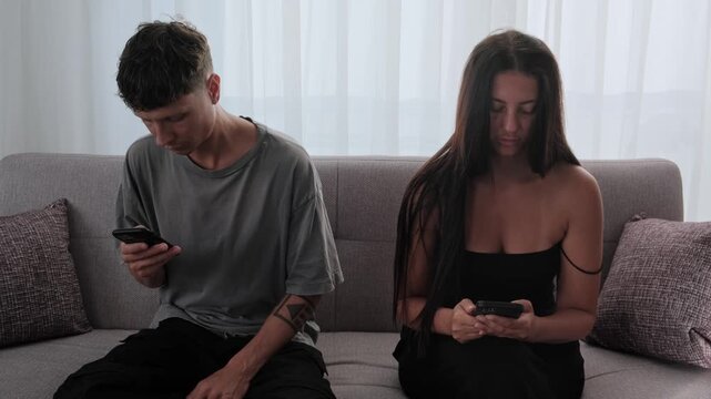 Couple ignoring each other while using smartphones on sofa, digital distraction, screen addiction, lack of communication and emotional distance in modern relationship