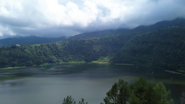 Aerial drone footage of Telaga Menjer, a beautiful volcanic lake located near the Dieng Plateau in Wonosobo, Central Java, Indonesia. Surrounded by lush green hills and spectacular mountain scenery