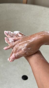Close-up of soapy hands washing with lather in a beautiful stone bathtub.