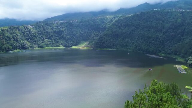 Aerial drone footage of Telaga Menjer, a beautiful volcanic lake located near the Dieng Plateau in Wonosobo, Central Java, Indonesia. Surrounded by lush green hills and spectacular mountain scenery