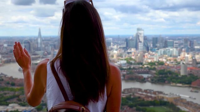 A woman with a backpack looks at the elevated view of the skyline of London, England, during a sunny summer day