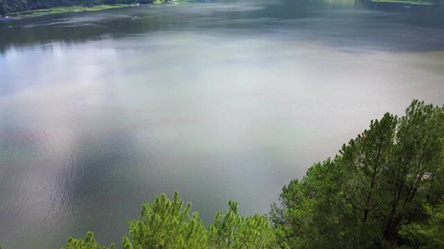 Aerial drone footage of Telaga Menjer, a beautiful volcanic lake located near the Dieng Plateau in Wonosobo, Central Java, Indonesia. Surrounded by lush green hills and spectacular mountain scenery