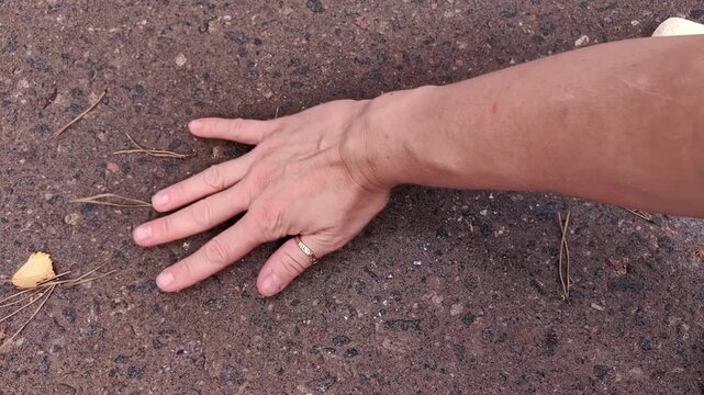 Adult hand resting on asphalt beside sidewalk chalk drawings, creative pause, outdoor art, summer hobby, simple composition.