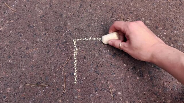 Adult hand drawing a square with sidewalk chalk on asphalt, creative outdoor activity, artistic design, summer recreation, education concept.