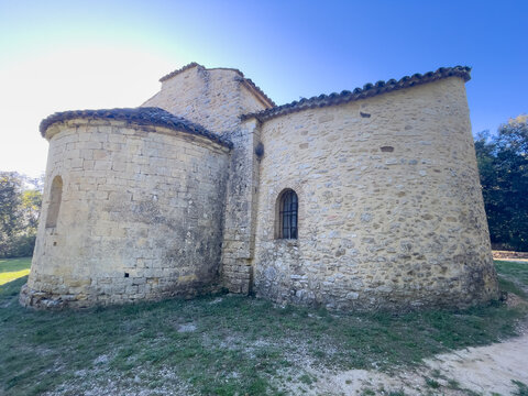 A wide-angle view of the exterior masonry walls and rounded apses of a historic medieval chapel, situated on a grassy area under a bright, clear blue sky.