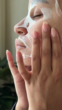 Young woman applying hydrating gold eye patches under her eyes in front of a mirror.