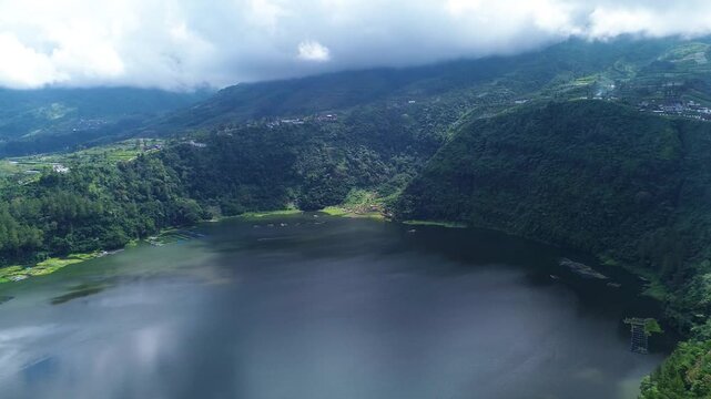 Aerial drone footage of Telaga Menjer, a beautiful volcanic lake located near the Dieng Plateau in Wonosobo, Central Java, Indonesia. Surrounded by lush green hills and spectacular mountain scenery