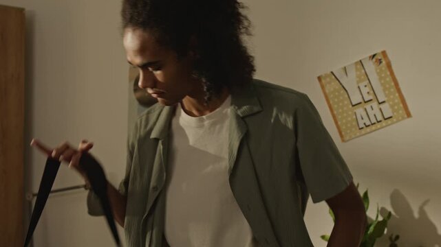 Handheld shot of Black teenager picking up smartphone and keys from desk, carrying duffel bag, and leaving room with suitcase. Footage represents student relocation, youth travel, or moving out themes