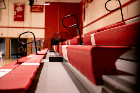 Wide view of empty school gymnasium with hardwood floor and retracted bleachers, illustrating education facilities, community gathering spaces, and multipurpose school environments.