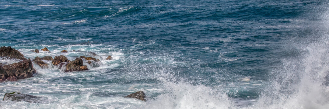 Ocean waves crashing against dark coastal rocks creating sea spray for a dramatic marine nature background