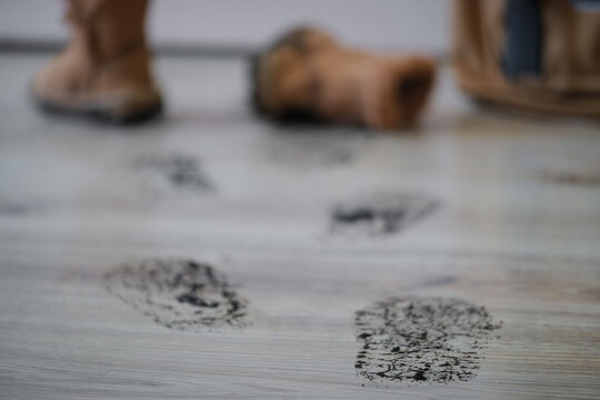 Close-up of muddy boot prints across a laminate floor inside a home, with dirty children's boots left near the entrance. Concept of rainy weather, household cleaning, dirty floors, home maintenance