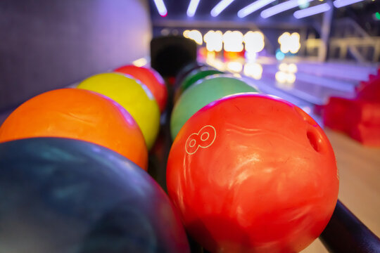 Row of colorful bowling balls on a rack in a club. Close-up of vibrant bowling equipment, featuring a red ball numbered eight, at an indoor center with neon lanes.
