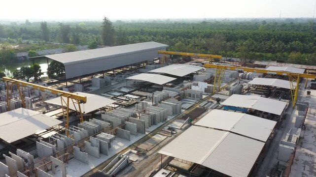 Large precast concrete panel manufacturing takes place within modern factory setting amidst expansive rural landscapes, utilizing cranes for efficient material handling operations.