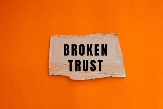 Broken trust concept with word on torn piece of paper on vibrant orange background, symbolizing betrayal and relationship issues