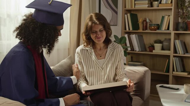 Medium shot of middle aged Caucasian mother crying with joy while holding framed diploma next to Black teenage graduate son. Clip is ideal for education marketing and family support campaigns