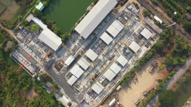 Precast Concrete modular buildings are under construction amidst rural setting with verdant vegetation and tranquil pond, showcasing innovative precast concrete wall panel development.