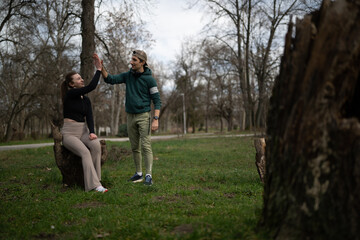 Naklejka premium A young man and woman give each other a high five while taking a break in a park. Casually dressed friends celebrate together during an outdoor walk amid leafless trees.