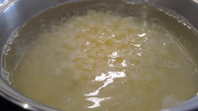 Boiling process of small white food particles forming in a pot of water, showcasing gradual changes in texture and appearance over time in a kitchen setting
