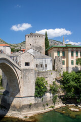 Obraz premium Scenic view showing the stone arch of the Stari Most (Old Bridge), the medieval Tara Tower, and the historic Cejvan Cehaja Madrasa in the old town of Mostar, Bosnia and Herzegovina.