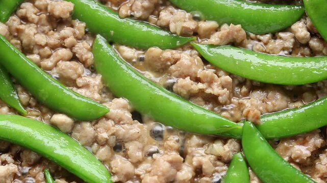 Stir-frying minced pork with fresh sugar snap peas in a hot pan. Top view shot