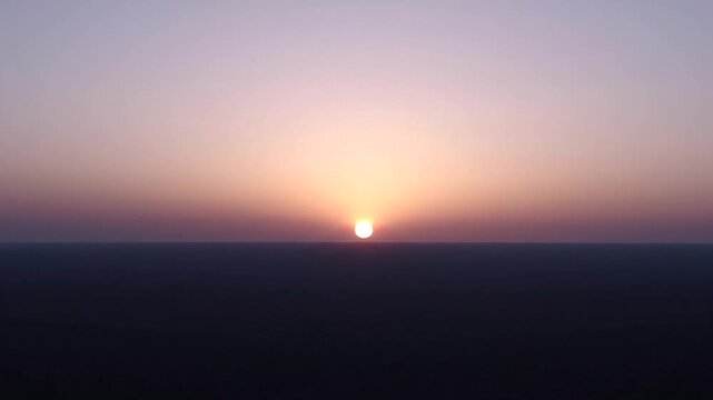 The bright sun rises over a dark and distant horizon line