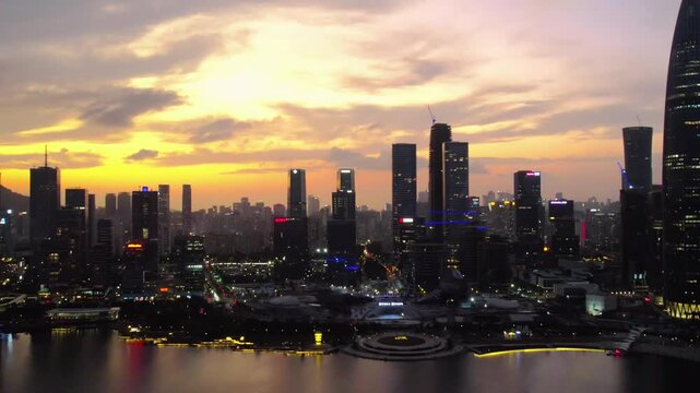A modern urban skyline at dusk, featuring tall buildings along a waterfront under a colorful sunset sky.
