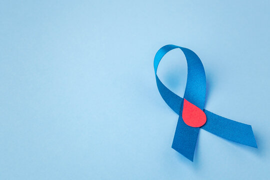 Blue ribbon with a red blood drop on a blue background with copy space, World Diabetes Day awareness concep