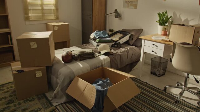 Full no people shot of cardboard boxes and open suitcase lying on bed in messy room, showing packing process for relocation. Perfect for moving services, real estate, student housing campaigns