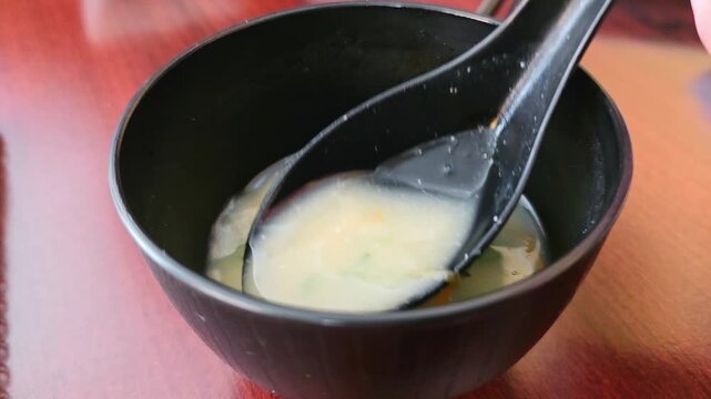 Spoon stirs a bowl of miso soup in a Japanese restaurant, warm broth.