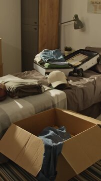 Vertical no people shot of packed suitcase, cardboard box, and clothes lying on bed in student bedroom. Footage is perfect for student relocation services, moving companies, or college campaigns