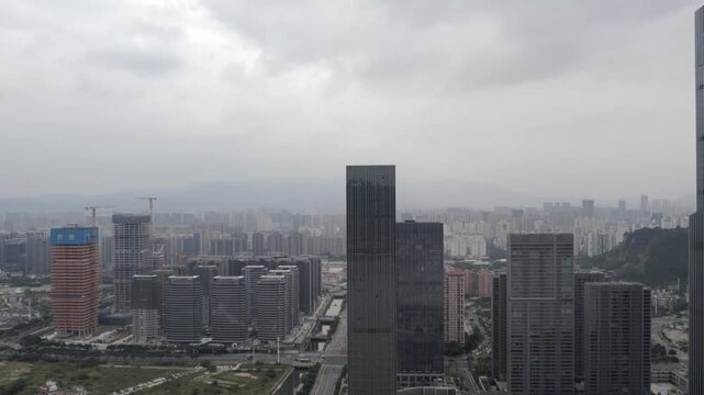 An elevated view of a modern urban district featuring tall skyscrapers under an overcast sky, with ongoing construction visible in the distance.