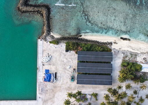 Aerial view of a solar panel array installed on a tropical island near a jetty and turquoise lagoon in Vaikaradhoo, Haa Dhaalu Atoll, Maldives.