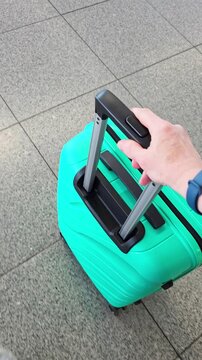Top-down view of hand pulling teal hard-shell suitcase across airport terminal floor, travel lifestyle, airport departure.