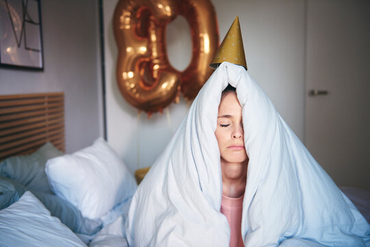Sad woman celebrating her birthday, sitting on bed under blanket