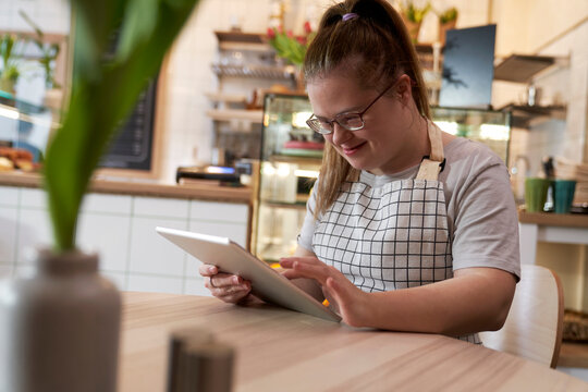 Smiling cafe owner with down syndrome using tablet PC at table in coffee shop