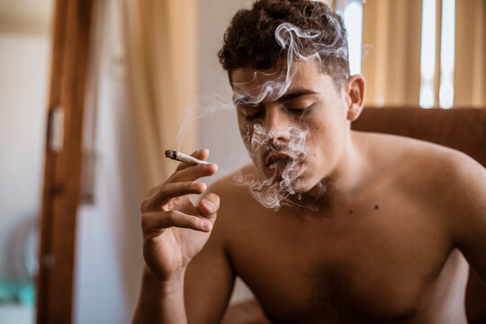 Barechested man smoking a joint of marijuana