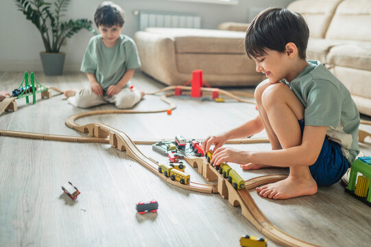 Smiling brothers play with wooden toy train on floor at home