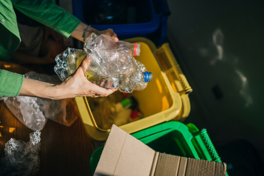 Hand sorting crushed plastic bottle into a recycling bin indoors
