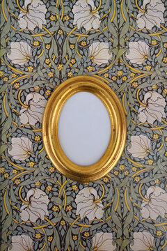 Oval golden picture frame on wallpaper with Art Nouveau floral design