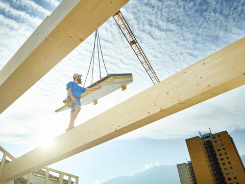 Young carpenter standing on purlin at construction site on sunny day