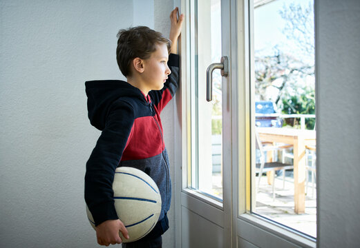 Sad boy with basketball looking out of window