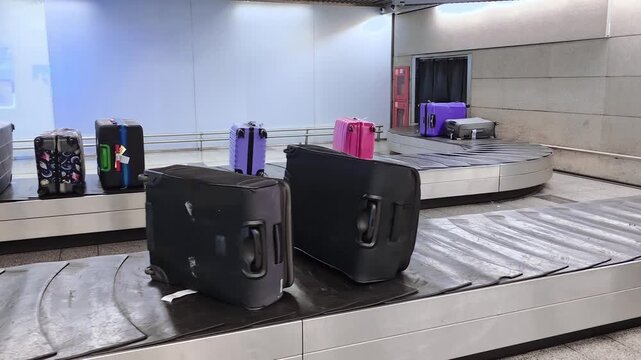 Suitcases of various colors rotating on airport baggage claim conveyor belt, passenger arrival, luggage collection, air travel.