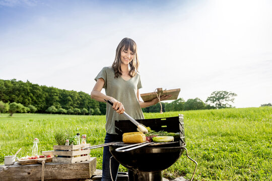 Smiling woman preparing vegetable on barbecue grill